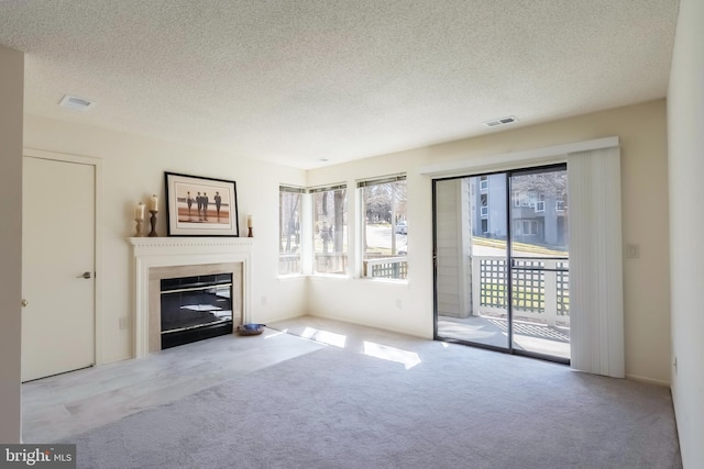 unfurnished living room with carpet floors, a glass covered fireplace, visible vents, and a textured ceiling