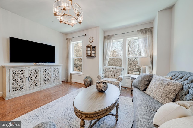 living room with a notable chandelier, wood finished floors, baseboards, and a healthy amount of sunlight