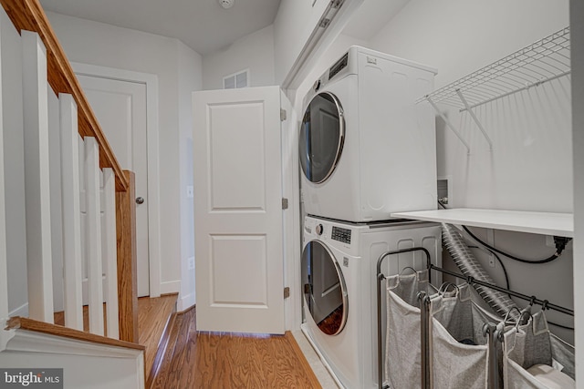 laundry room with laundry area, stacked washer and dryer, light wood-style flooring, and visible vents