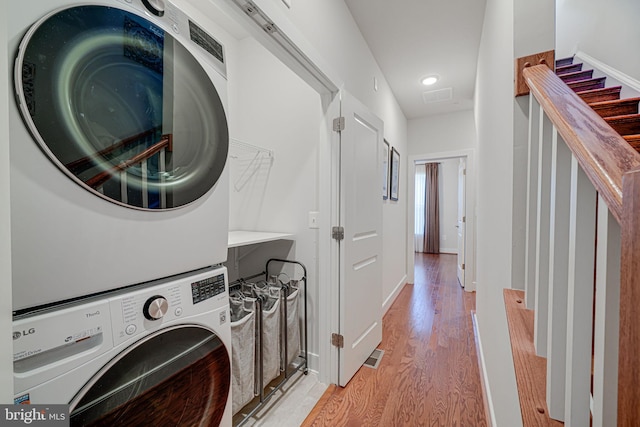 laundry room featuring laundry area, light wood-style flooring, stacked washing maching and dryer, and baseboards