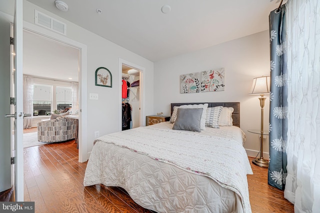 bedroom with visible vents, a walk in closet, baseboards, a closet, and wood-type flooring