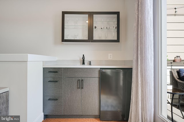 bar featuring wood finished floors, stainless steel dishwasher, fridge, and a sink