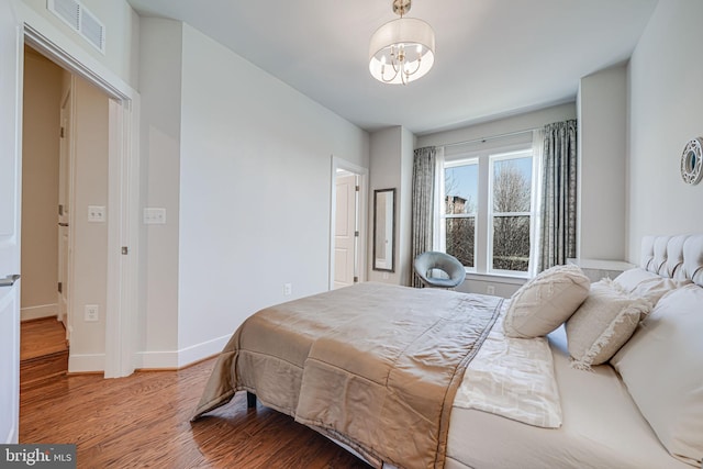 bedroom with a chandelier, visible vents, baseboards, and wood finished floors