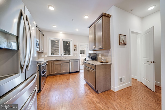 kitchen with visible vents, a sink, appliances with stainless steel finishes, light wood finished floors, and decorative backsplash