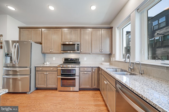 kitchen with light wood-style flooring, a sink, backsplash, stainless steel appliances, and light stone countertops