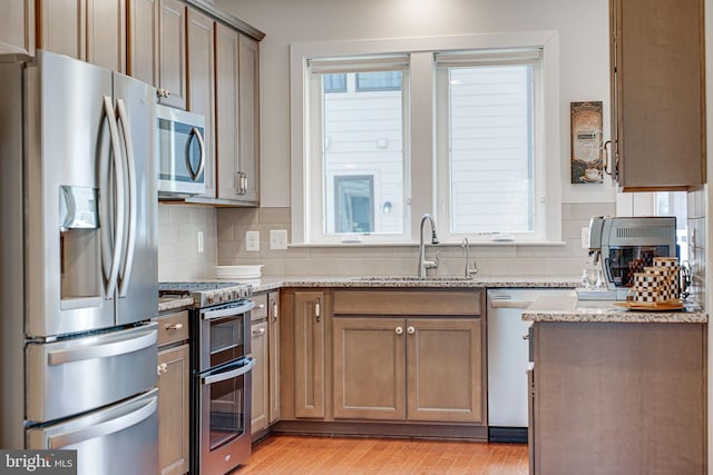 kitchen featuring light stone counters, light wood-style flooring, a sink, appliances with stainless steel finishes, and backsplash