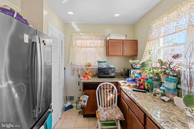 kitchen with visible vents, appliances with stainless steel finishes, light tile patterned flooring, brown cabinetry, and light stone countertops