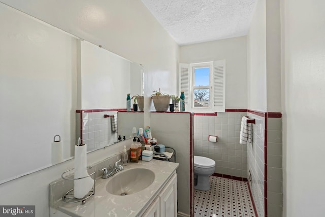 bathroom with vanity, a wainscoted wall, a textured ceiling, tile walls, and toilet