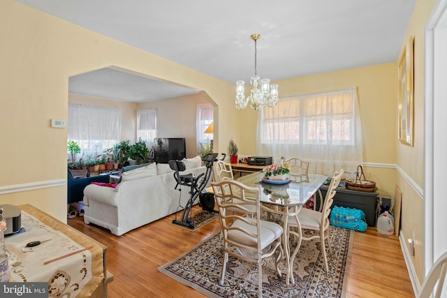 dining space featuring arched walkways, a notable chandelier, and wood finished floors