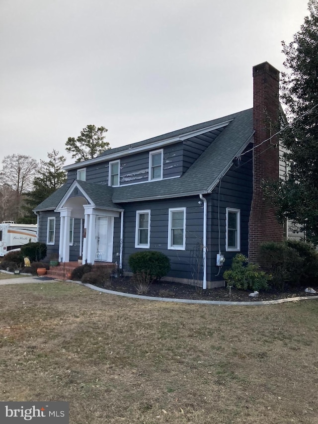 view of front of house featuring a shingled roof, a chimney, and a front lawn