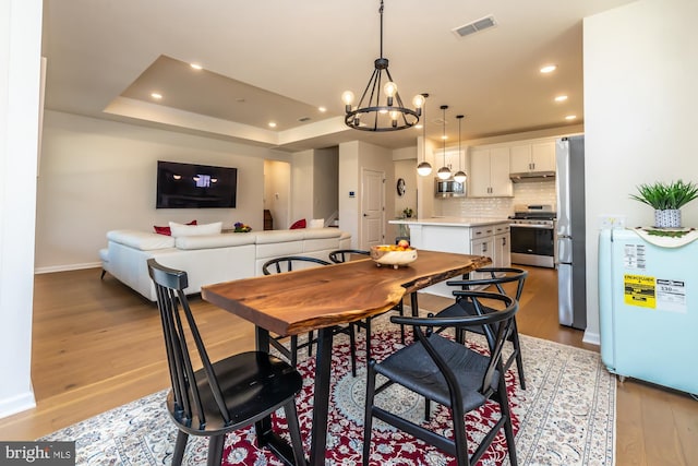 dining room featuring light wood-type flooring, visible vents, a raised ceiling, and recessed lighting