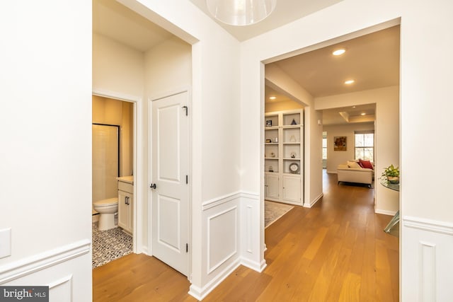 hall with light wood-style floors, recessed lighting, wainscoting, and a decorative wall