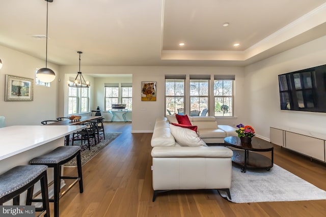 living room with dark wood-style flooring, recessed lighting, a raised ceiling, ornamental molding, and baseboards