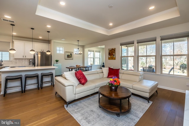 living room with light wood-style floors, visible vents, a raised ceiling, and a wealth of natural light