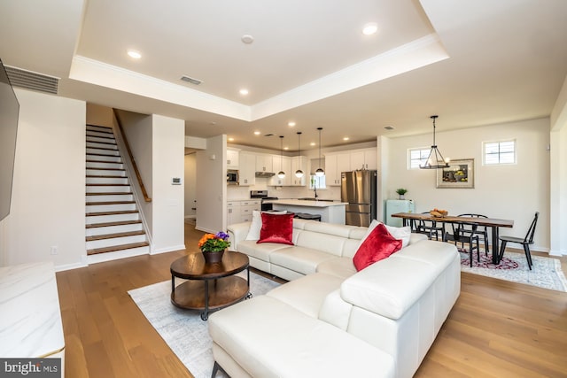 living room featuring stairs, recessed lighting, a raised ceiling, and light wood-style floors