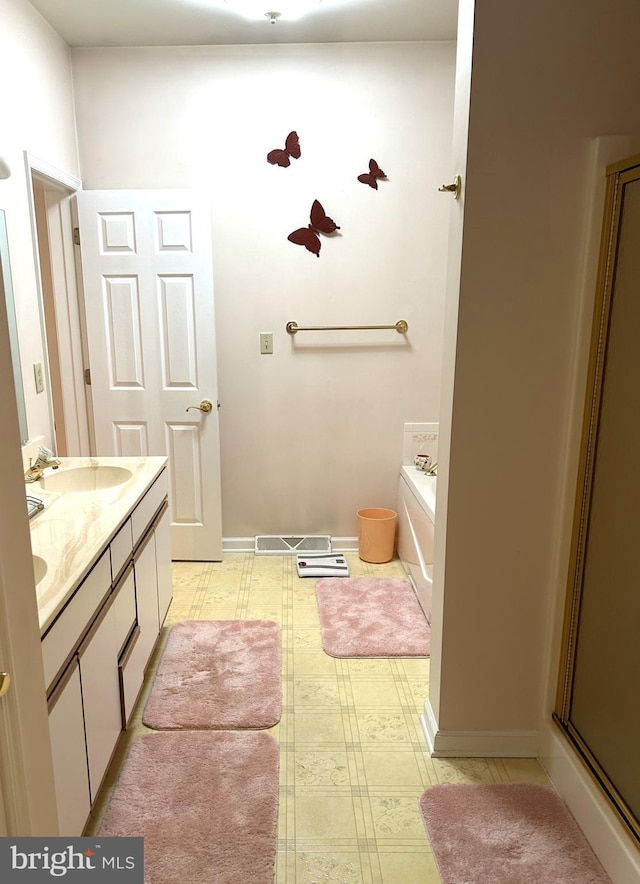 bathroom with double vanity, a sink, a bath, baseboards, and tile patterned floors