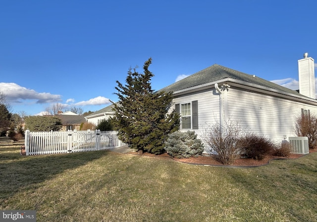 view of side of property with a yard, central AC unit, a chimney, and fence