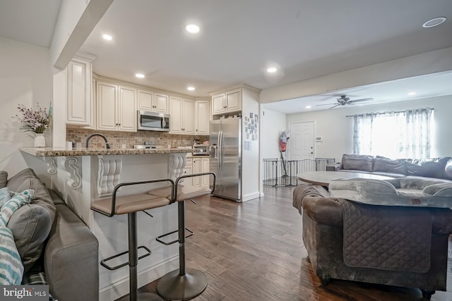 kitchen with a breakfast bar area, a peninsula, open floor plan, appliances with stainless steel finishes, and decorative backsplash