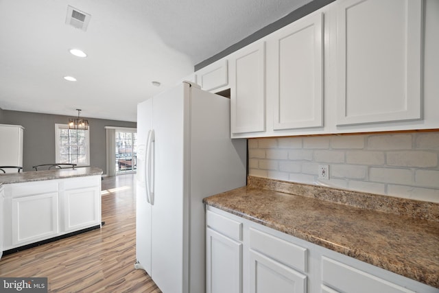 kitchen with light wood-style floors, white refrigerator with ice dispenser, visible vents, and white cabinets