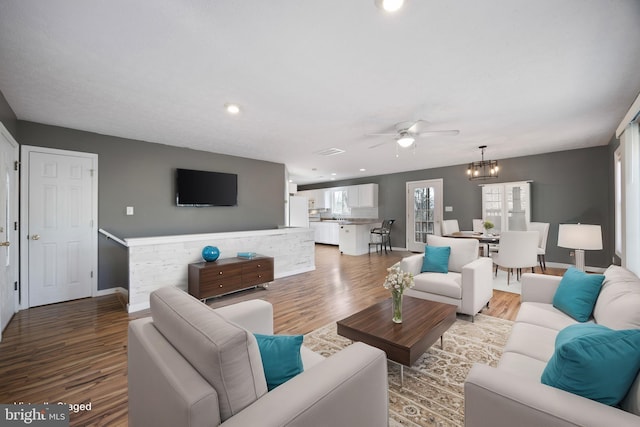 living area with baseboards, wood finished floors, and ceiling fan with notable chandelier