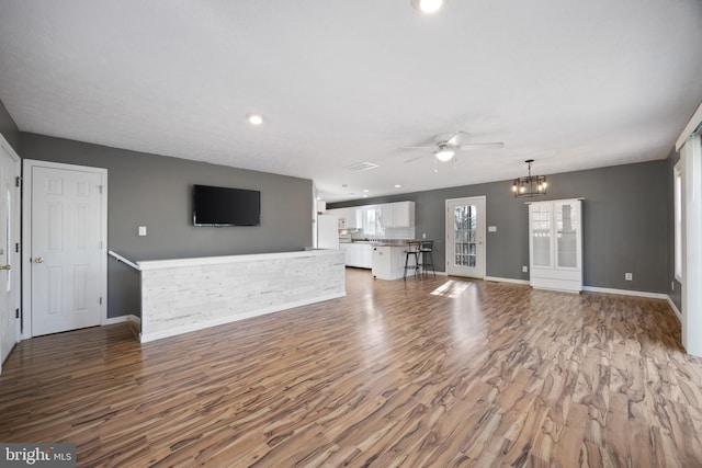 unfurnished living room with ceiling fan with notable chandelier, wood finished floors, and baseboards