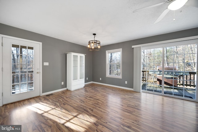 unfurnished dining area featuring ceiling fan with notable chandelier, wood finished floors, visible vents, and baseboards