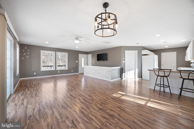 unfurnished living room featuring ceiling fan with notable chandelier, recessed lighting, baseboards, and wood finished floors