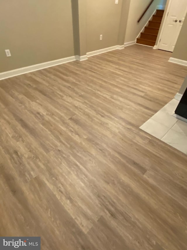 unfurnished living room featuring stairway, wood finished floors, and baseboards