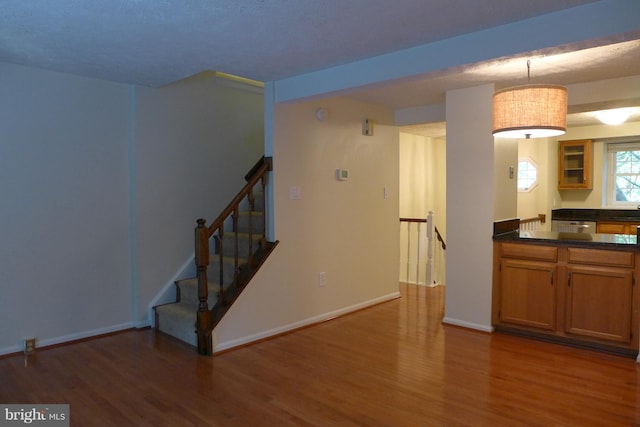 kitchen with wood finished floors, baseboards, hanging light fixtures, brown cabinets, and dark countertops