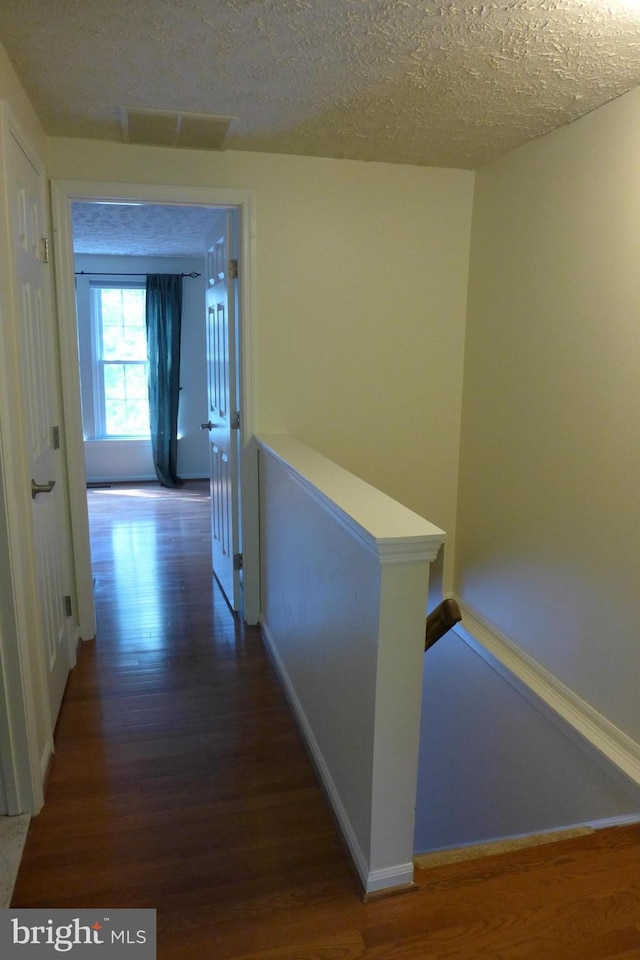 hallway featuring baseboards, visible vents, wood finished floors, a textured ceiling, and an upstairs landing