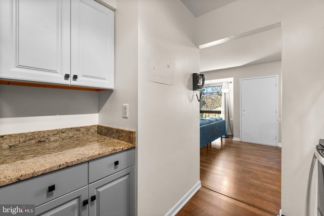 kitchen featuring light stone countertops, baseboards, electric panel, dark wood-style flooring, and white cabinets