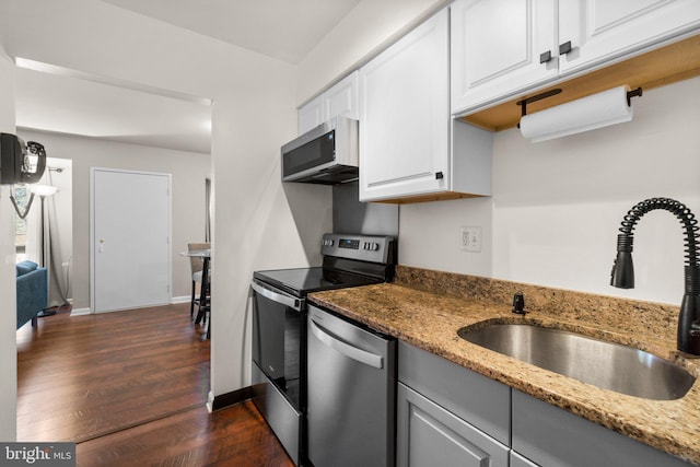 kitchen featuring a sink, stainless steel appliances, light stone countertops, and dark wood-type flooring