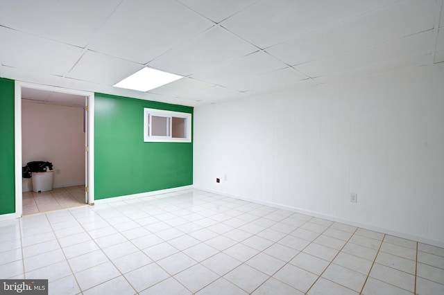 spare room featuring light tile patterned floors, a drop ceiling, and baseboards
