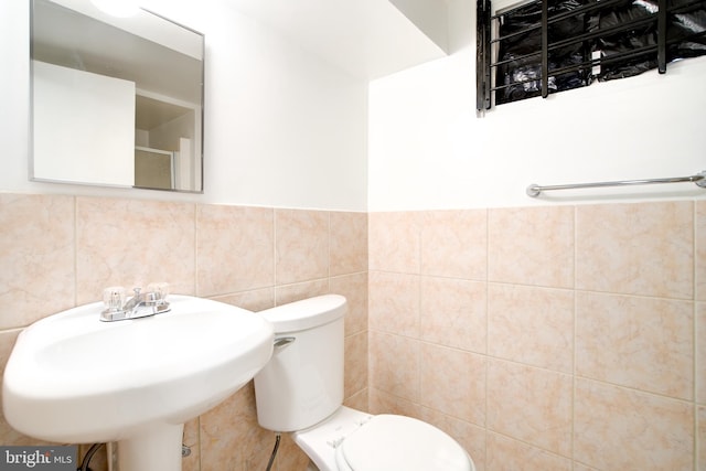 bathroom featuring a sink, toilet, and tile walls