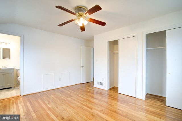 unfurnished bedroom featuring visible vents, lofted ceiling, light wood-style floors, multiple closets, and connected bathroom
