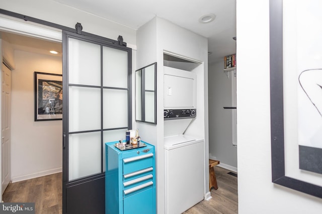 laundry room featuring stacked washer and dryer, a barn door, wood finished floors, and laundry area