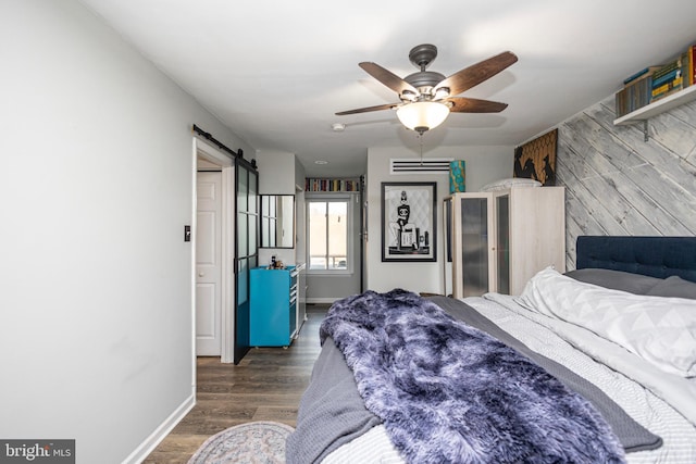 bedroom with a barn door, ceiling fan, wood walls, wood finished floors, and baseboards