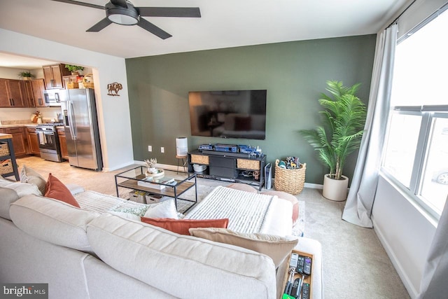 living area with baseboards, light carpet, and a ceiling fan