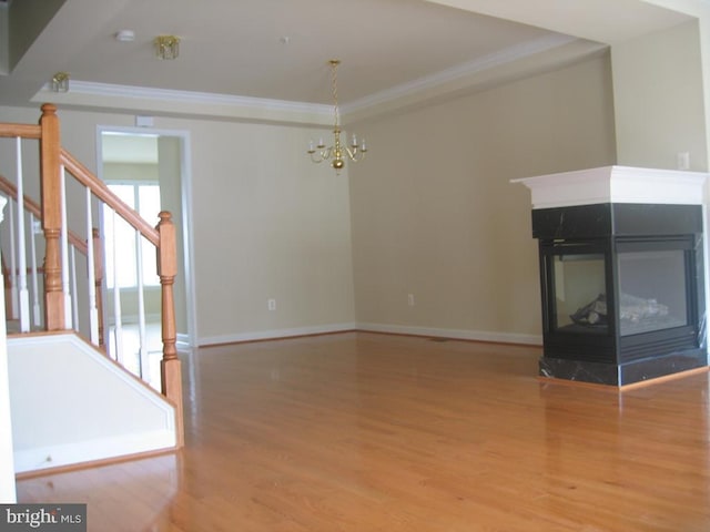 unfurnished living room featuring wood finished floors, stairway, a multi sided fireplace, and crown molding