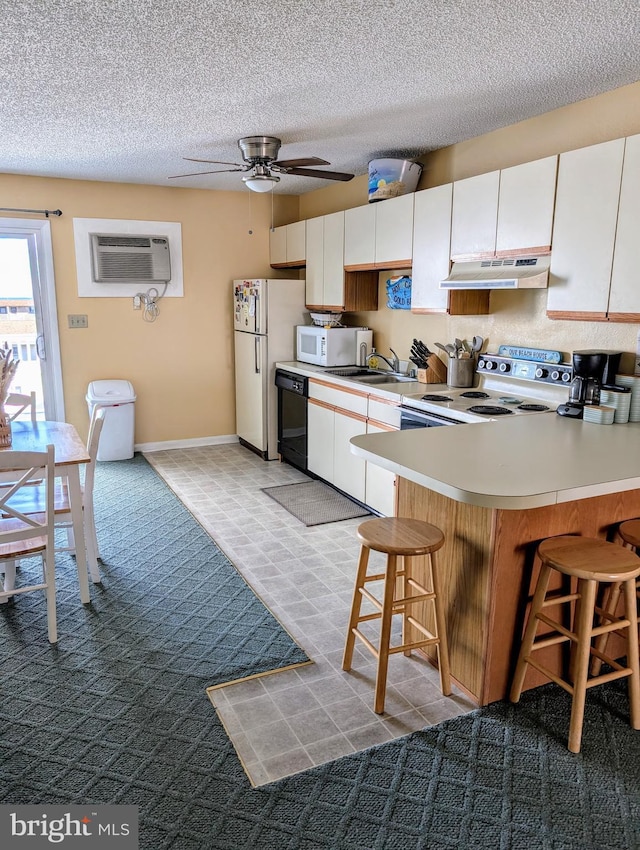 kitchen with a breakfast bar area, under cabinet range hood, white appliances, an AC wall unit, and light countertops