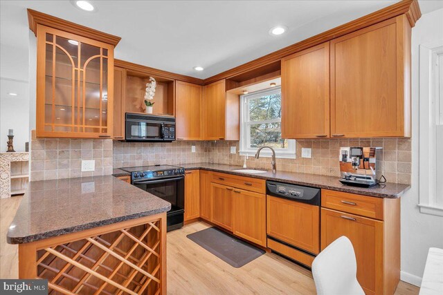 kitchen with decorative backsplash, black appliances, light wood-style flooring, and a sink