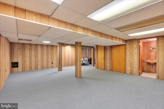 finished below grade area with a sink, a paneled ceiling, wood walls, and carpet flooring