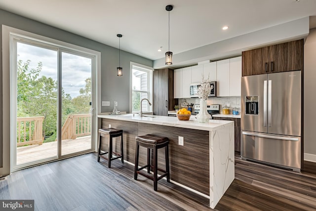 kitchen featuring dark wood-style floors, a breakfast bar, tasteful backsplash, appliances with stainless steel finishes, and a sink