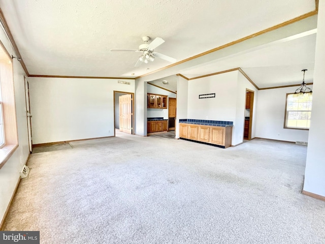 unfurnished living room featuring ceiling fan with notable chandelier, ornamental molding, and light colored carpet