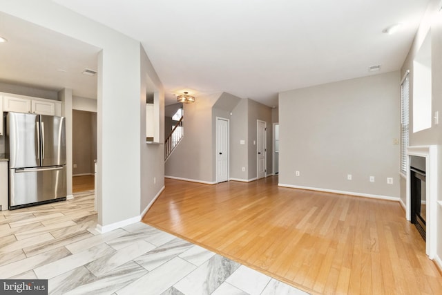 unfurnished living room featuring visible vents, baseboards, stairs, light wood-type flooring, and a glass covered fireplace