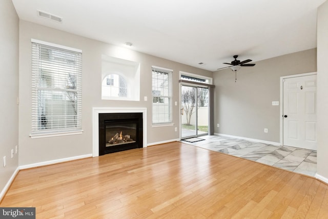 unfurnished living room with baseboards, visible vents, a ceiling fan, a glass covered fireplace, and wood finished floors