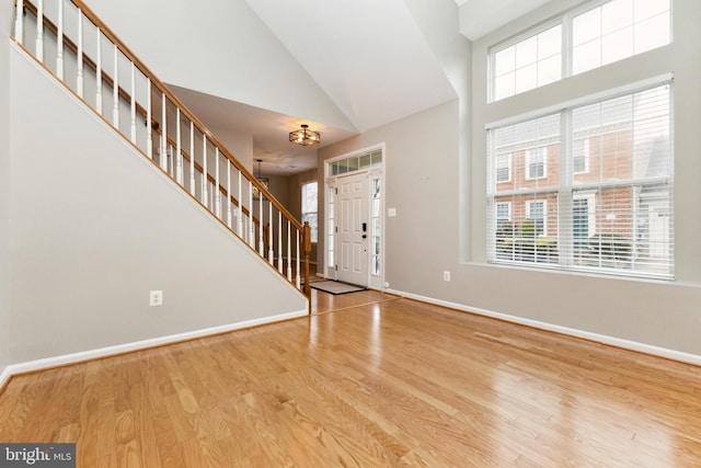 foyer entrance featuring high vaulted ceiling, stairway, wood finished floors, and baseboards