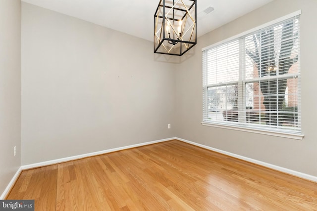 spare room with an inviting chandelier, wood finished floors, and baseboards