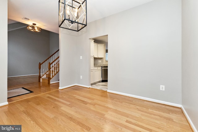 unfurnished dining area with visible vents, an inviting chandelier, light wood-type flooring, baseboards, and stairs