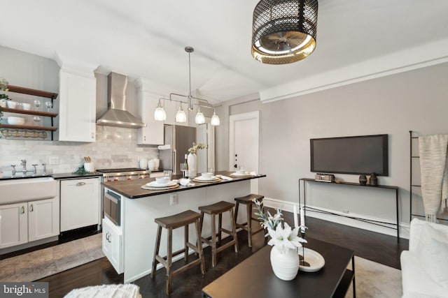 kitchen featuring stainless steel appliances, dark countertops, decorative backsplash, a sink, and wall chimney exhaust hood